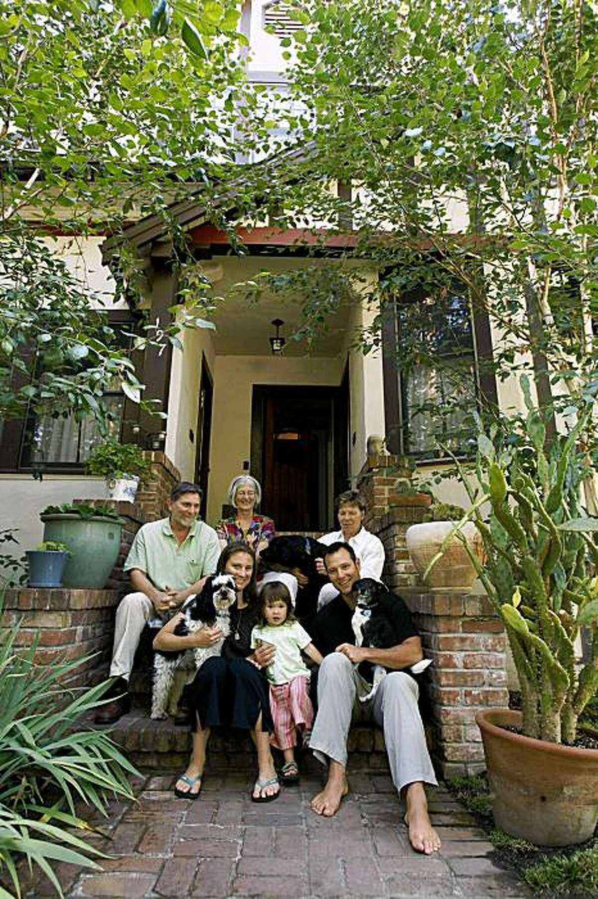 Ben Ladomirak, bottom right, sits with his family, daughter Lleu (cq) , 2, left, wife, Jesse, far left bottom, Jesse's parents, Bob Fletcher, left, and Marguerite Fletcher, above Jesse, and Ben's mother, Sylvia Seibert, top right, along with dogs, Checker in Jesse's arms, Mason in Ben's arms and Diva in Sylvia's arms, on the stairs outside their three unit Palo Alto property Friday morning, July 17, 2009.