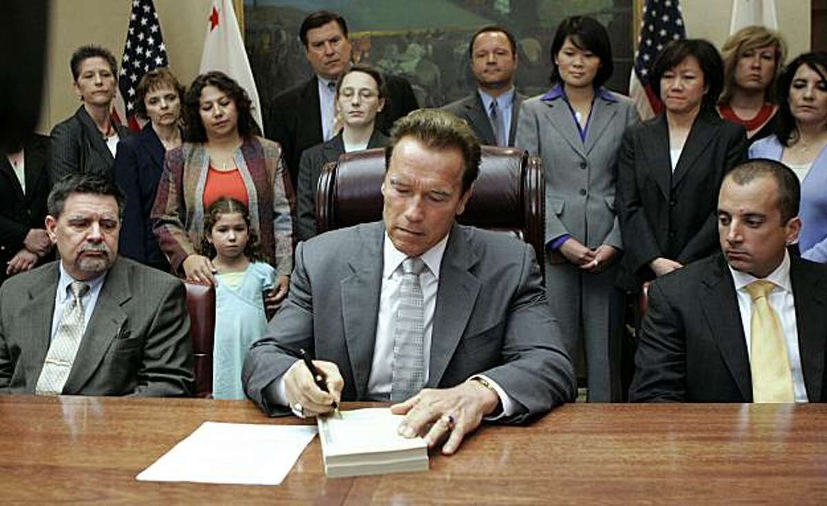 Gov. Arnold Schwarzenegger signs the $85 billion revised state budget as Finance Director Mike Genest, seated left, and Legislative Secretary Michael Prosio, seated right, look on during ceremonies at the Capitol in Sacramento, Calif., Tuesday, July 28, 2009. (AP Photo/Rich Pedroncelli)