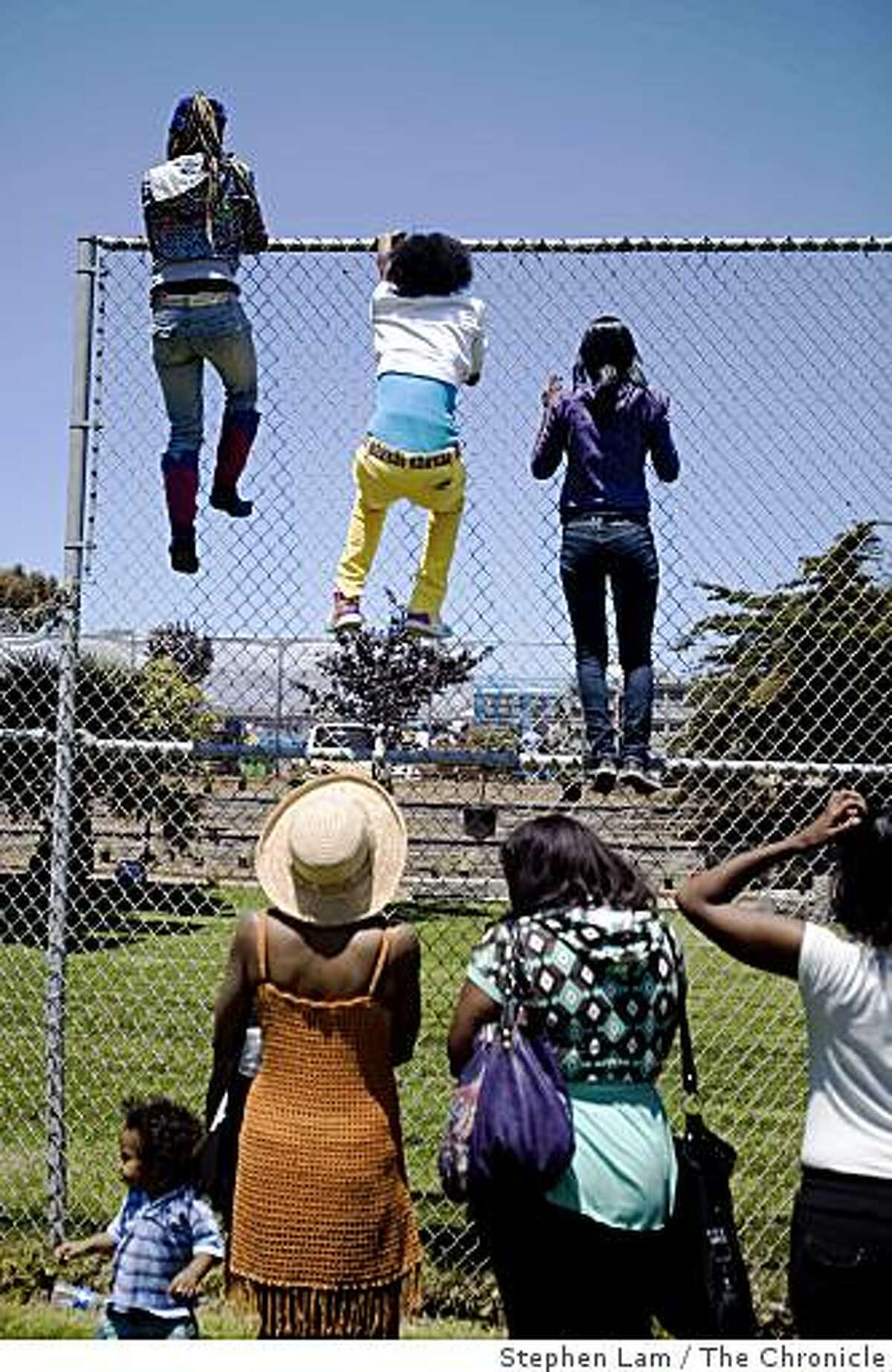 From left, Linda Williams, Valinda Willams, and Yoshika Coleham, climbs a fence in an effort to get a glimpse of First Lady Michelle Obama and California first lady Maria Shriver inside Bret Harte Elementary School in San Francisco, Calif. on Monday June 22, 2009.