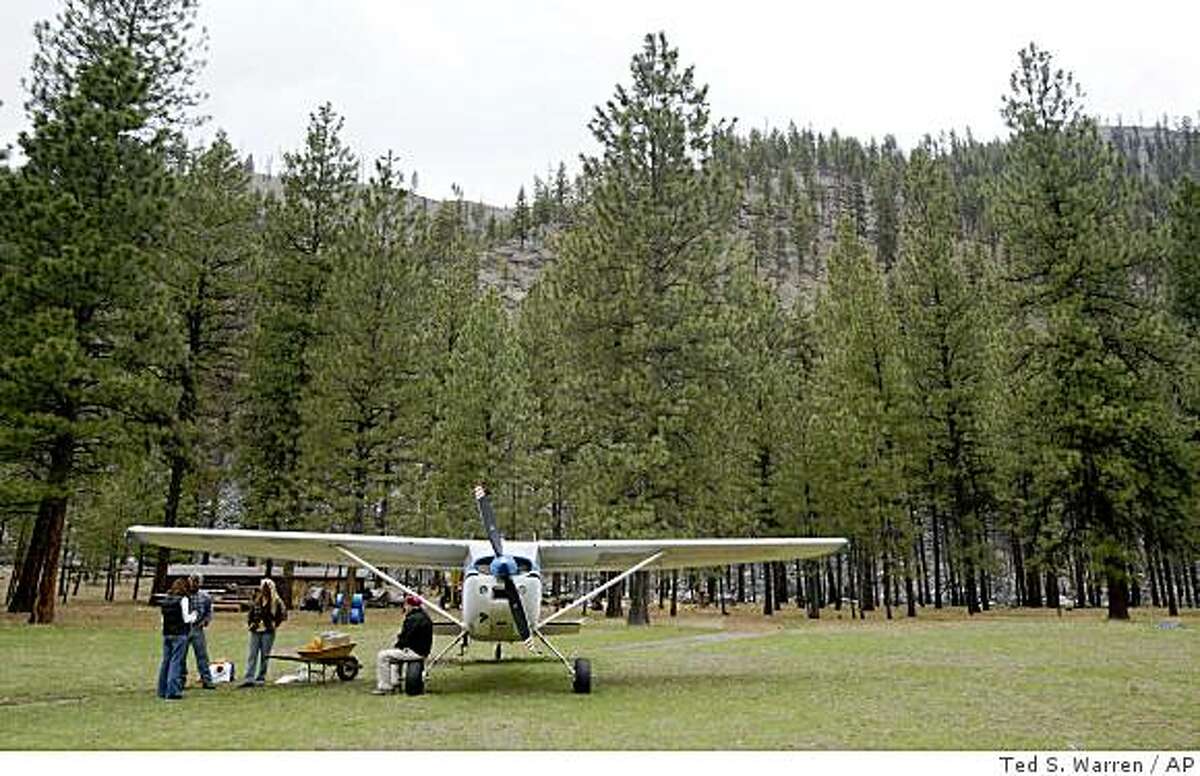 In this April 15, 2009 photo, Ray Arnold sits on the wheel of the Cessna 185 airplane he uses to deliver mail and other supplies to the remote Idaho backcountry, as he visits with Greg Metz and Sue Anderson, caretakers of the Yellow Pine Bar property near the Salmon River in central Idaho's Frank Church-River of No Return Wilderness. Arnold flies the only backcountry air mail route left in the lower 48 states, delivering mail to nearly two dozen ranches on a stretch of land larger than Indiana. (AP Photo/Ted S. Warren)