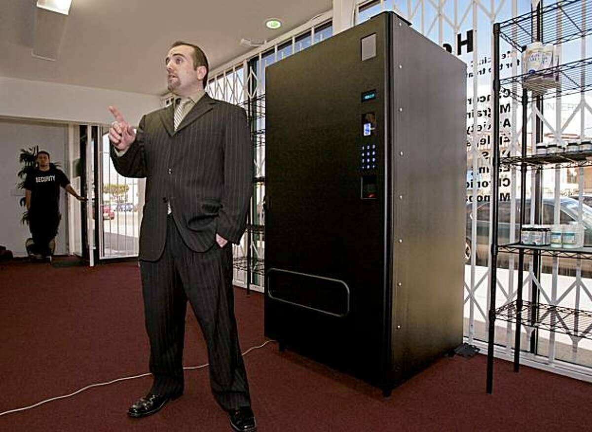 Los Angeles medical-cannabis dispensary owner Vincent Mehdizadeh poses with his new Marijuana vending machine installed at the Herbal Nutrition Center in Los Angeles, Tuesday, Jan. 29, 2008. The black, armored machine is bolted to the floor dispenses medical-cannabis to patients who provide a doctor's prescription and special identification card and their fingerprints. (AP Photo/Damian Dovarganes)