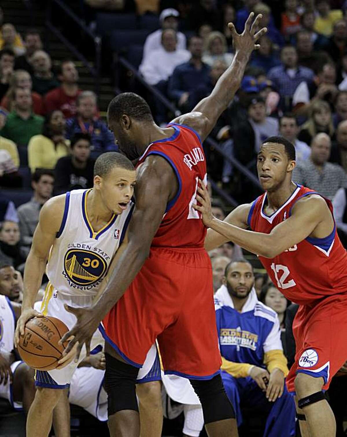 Golden State Warriors' Stephen Curry, left, looks for a way around Philadelphia 76ers' Elton Brand (42) and Evan Turner (12) during the first half of an NBA basketball game Monday, Dec. 27, 2010, in Oakland, Calif.