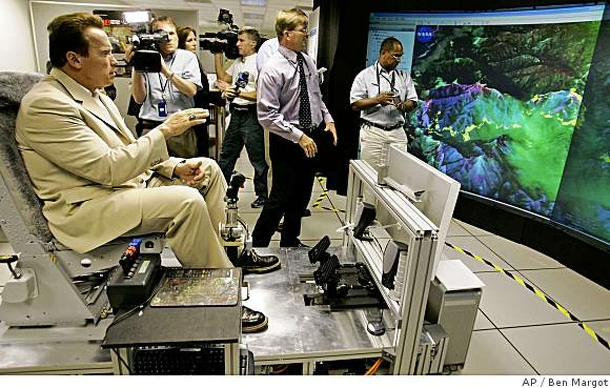 California Gov. Arnold Schwarzenegger, left, gestures as he sits in a flight simulator while viewing aerial infrared images of fire areas in California provided by Steve Hipskind, Chief of the NASA Earth Science Division, at the NASA Ames Research Center in Moffett Field, Calif., Monday, July 14, 2008. Schwarzenegger and fire officials toured the facility to discuss the important role of NASAs remotely piloted aircraft, named Ikhana, played in Californias wildfire fight. The unmanned aircraft carrying a NASA infrared scanning sensor flew over much of the state this past week, gathering information that was delivered to fire commanders in the field, helping them understand the terrain and behavior of the states most dangerous fires. (AP Photo/Ben Margot)