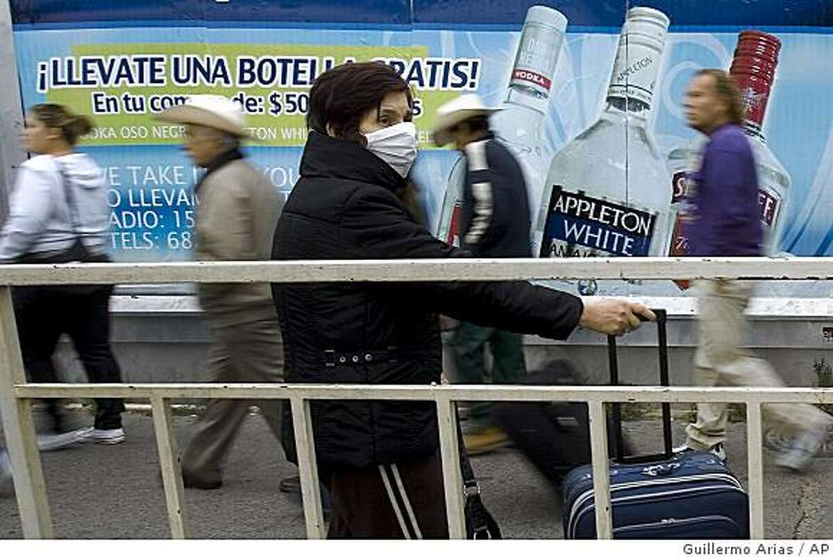A woman wears a surgical mask as people line up at the US-Mexico border crossing in Tijuana, Mexico, Tuesday, April 28, 2009. At least five people have been hospitalized with swine flu in the United States and deaths are likely, a U.S. health official said Tuesday. In Mexico, more than 150 deaths were believed to have been caused by swine flu.