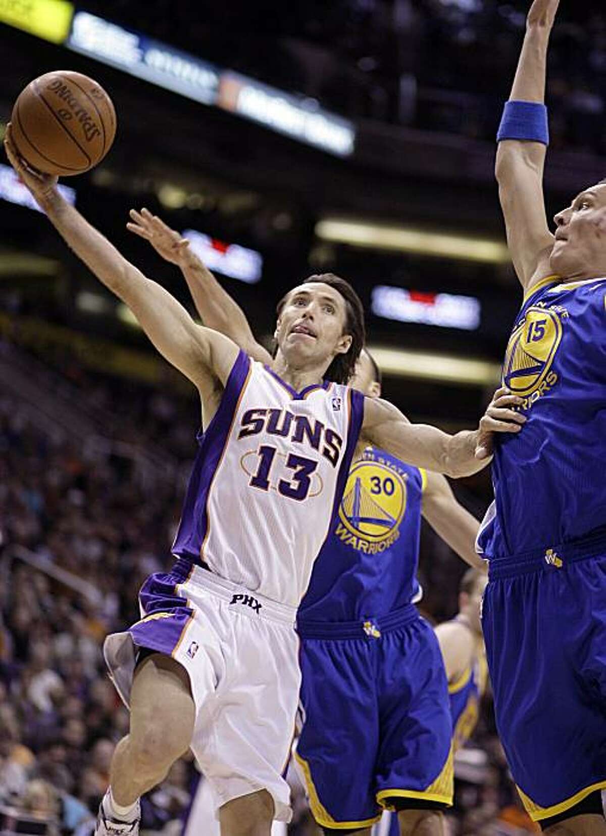 Phoenix Suns guard Steve Nash, left, drives past Golden State Warriors center Andris Biedrins, right, of Latvia, and guard Stephen Curry, rear, on his way to the basket in the second quarter of an NBA basketball game Thursday, Feb. 10, 2011, in Phoenix.