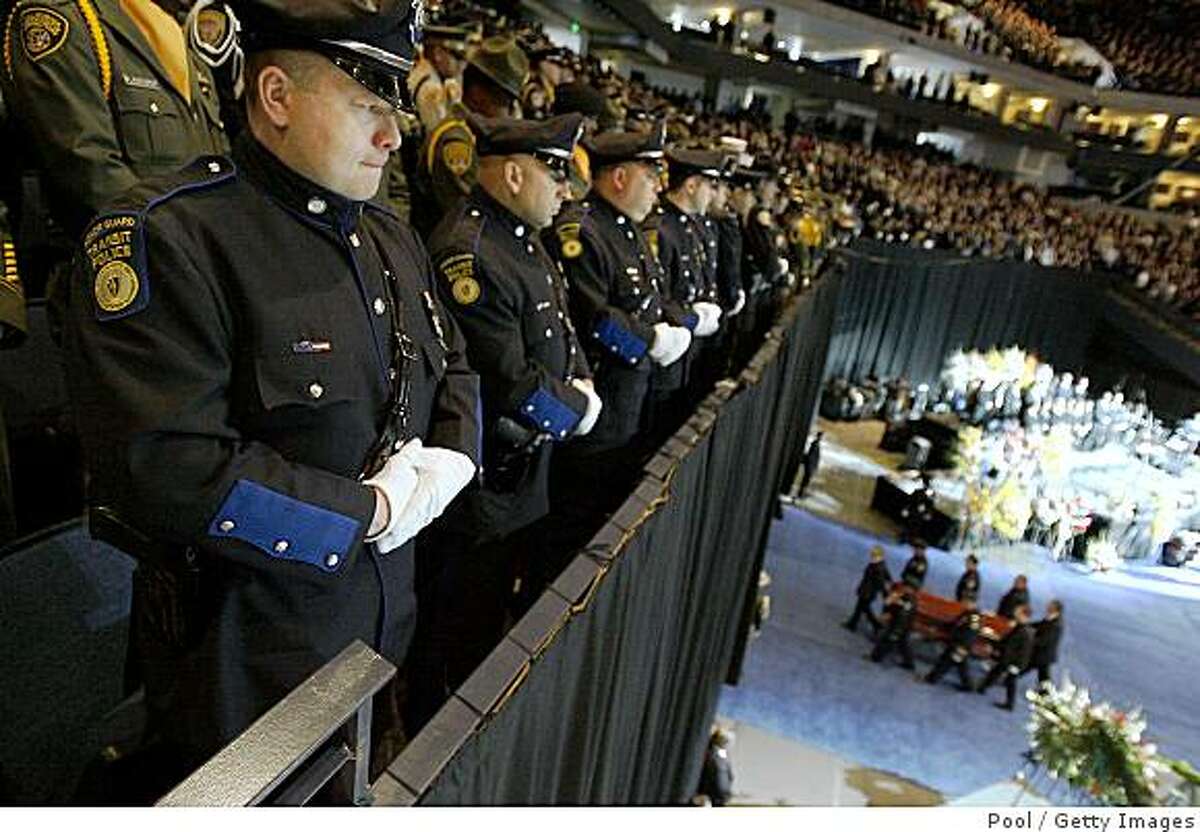 OAKLAND, CA - MARCH 27: Massachusetts Transit Police Officer Steve O'Hara (L) stands at attention as the caskets of Oakland Police Officers Sgt. Mark Dunakin, 40; John Hege, 41; Sgt. Ervin Romans, 43; and Sgt. Daniel Sakai, 35, are carried from the Oracle Arena on March 27, 2009 in Oakland, California. Thousands of police officers from across the country joined other mourners to pay their respects to the four officers killed in the line of duty March 21 following a traffic stop of a fugitive parolee. (Photo by Tony Avelar-Pool/Getty Images)