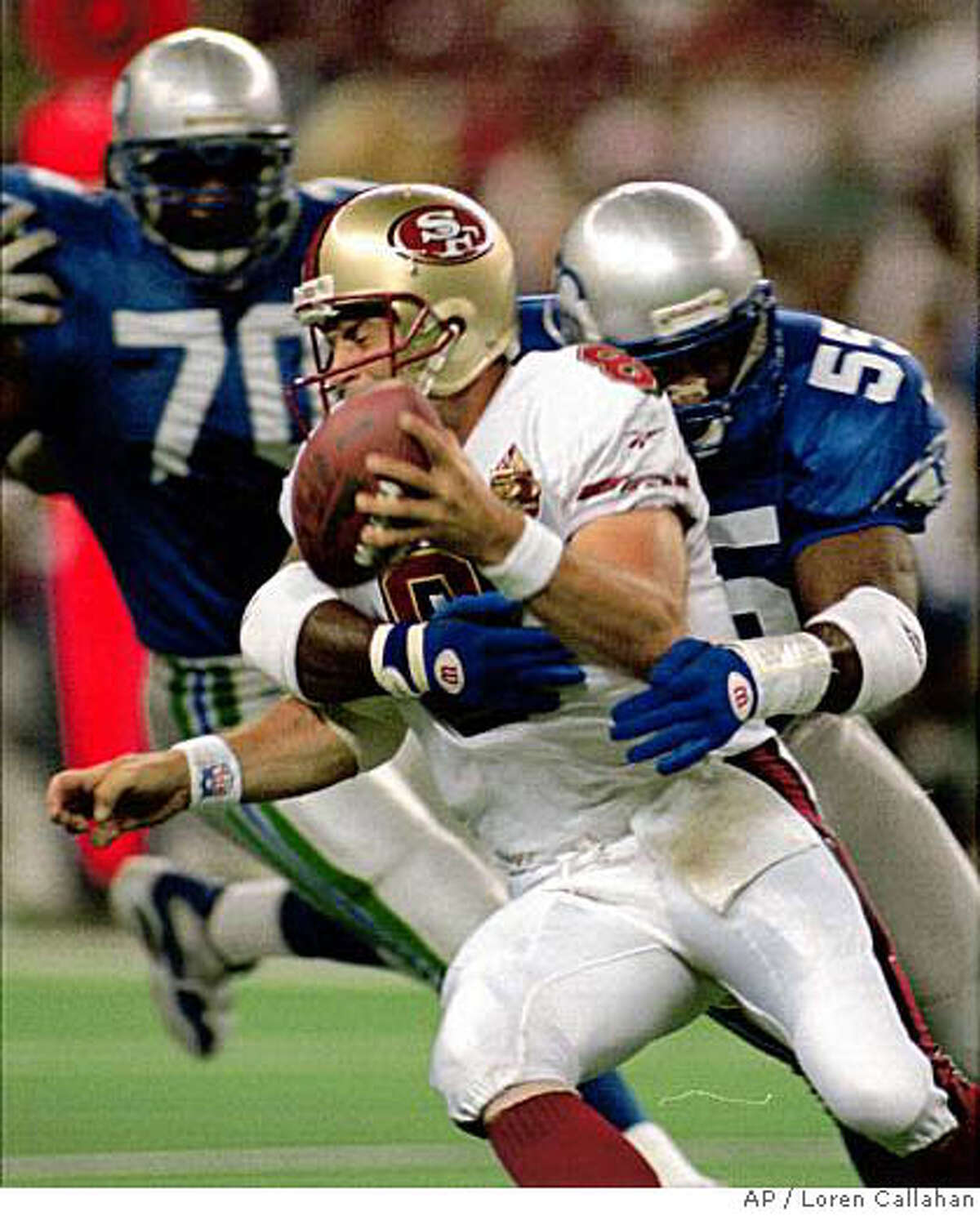 San Francisco 49ers quarterback Steve Young is wrapped-up in an early first-quarter sack by Seattle Seahawks' Winston Moss, as teammate Michael Sinclair (70) moves in Friday, Aug. 23, 1996 in Seattle. Young was tagged for a nine-yard loss on the play. (AP Photo/Loren Callahan)