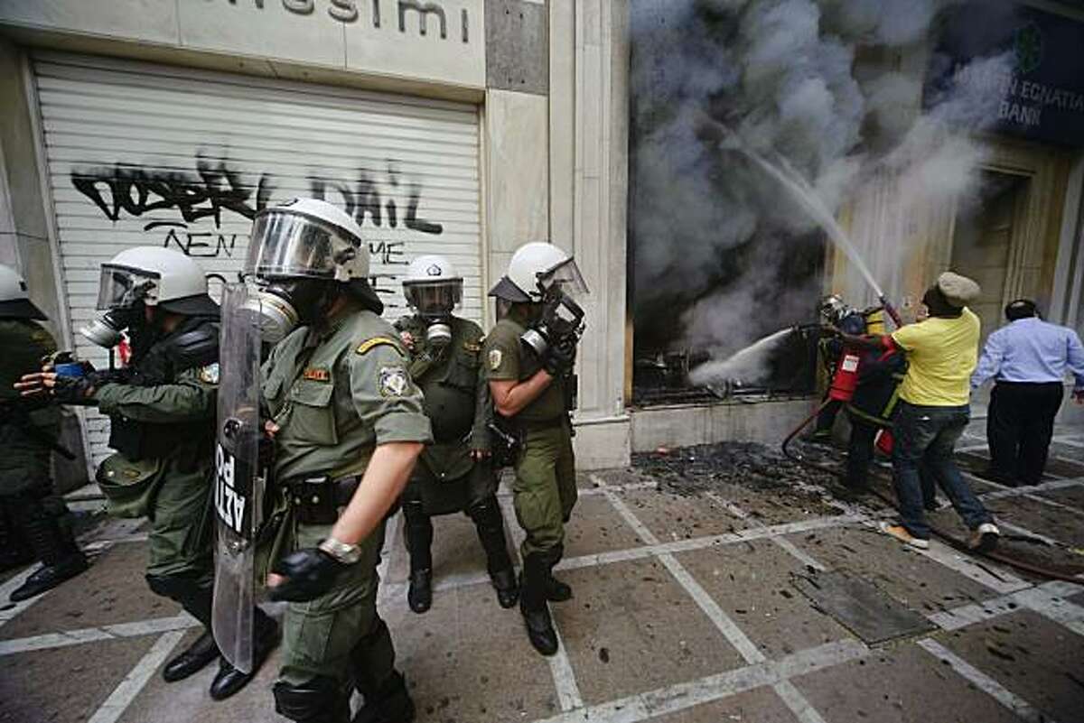 Riot police stands next to a burning Marfin Egnatia Bank, where three people died, in central Athens, Wednesday, May 5, 2010. Greek fire officials say three people died in a blaze that broke out at an Athens bank during rioting over government austerity measures. An estimated 100,000 people took to the streets Wednesday during a nationwide wave of strikes against spending cuts aimed at saving the country from bankruptcy