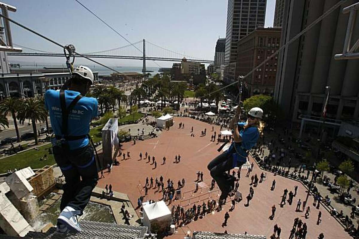 2010 gold medalists american speed skater Shani Davis (left) takes a leap as Canadian ski cross racer Ashleigh McIvor (right) watches on the zipline at Justin Herman Plaza in San Francisco, Calif., on Thursday, April 8, 2010. They launch an 11 day event called "The British Columbia Experience" which includes this 600 ft. urban zipline ride.