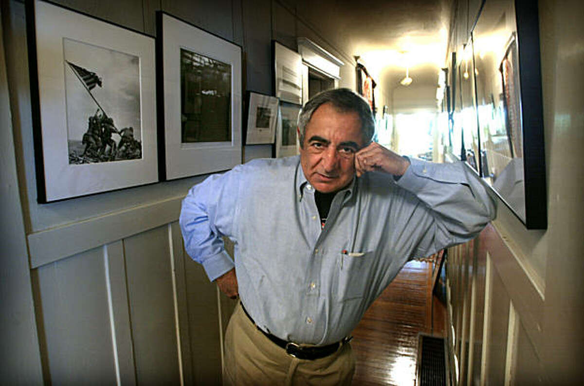 Photographer Jim Marshall in the hallway of his home. He has dedicated the entire wall (at left) to displaying the work of other photographers he has met and in some cases has traded photos with.