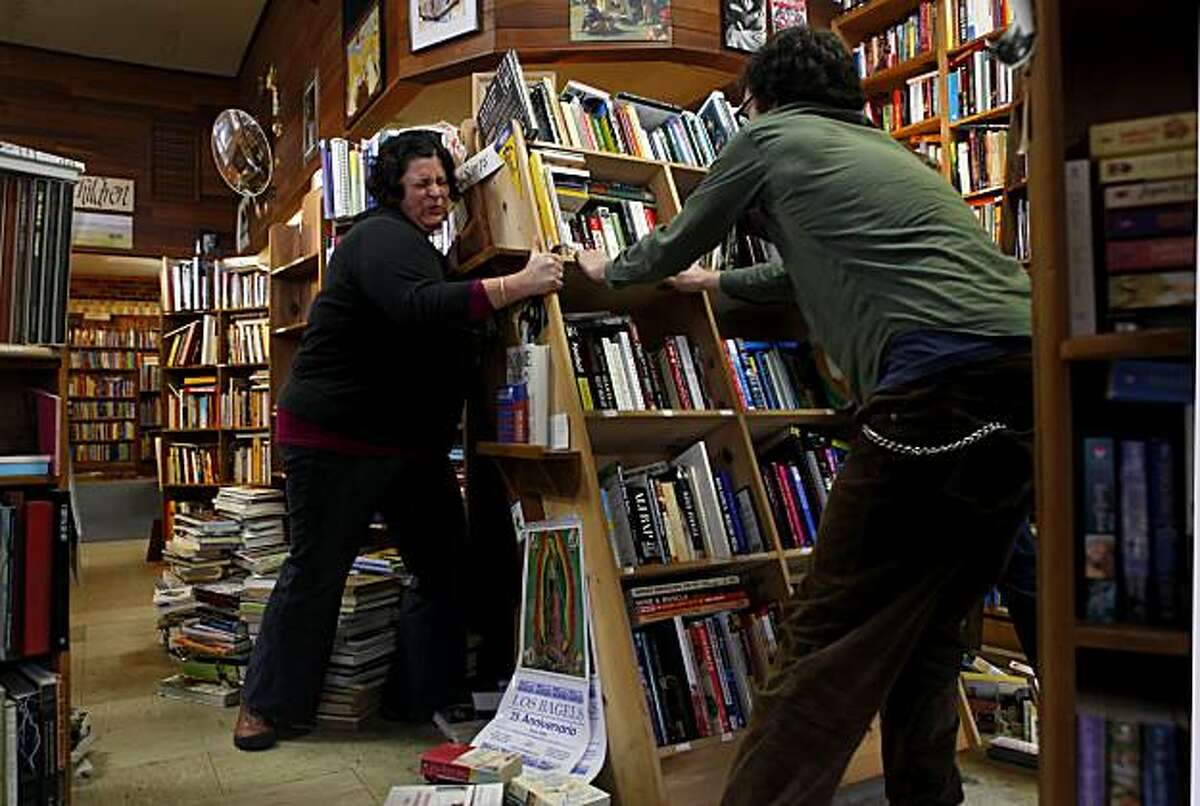 Gabriella Aragon, left, and Aber Miller lift a collapsed bookshelf Sunday at the Booklegger in Eureka. The Booklegger lost four big windows and several bookshelves were knocked over during Saturday's 6.5 earthquake.