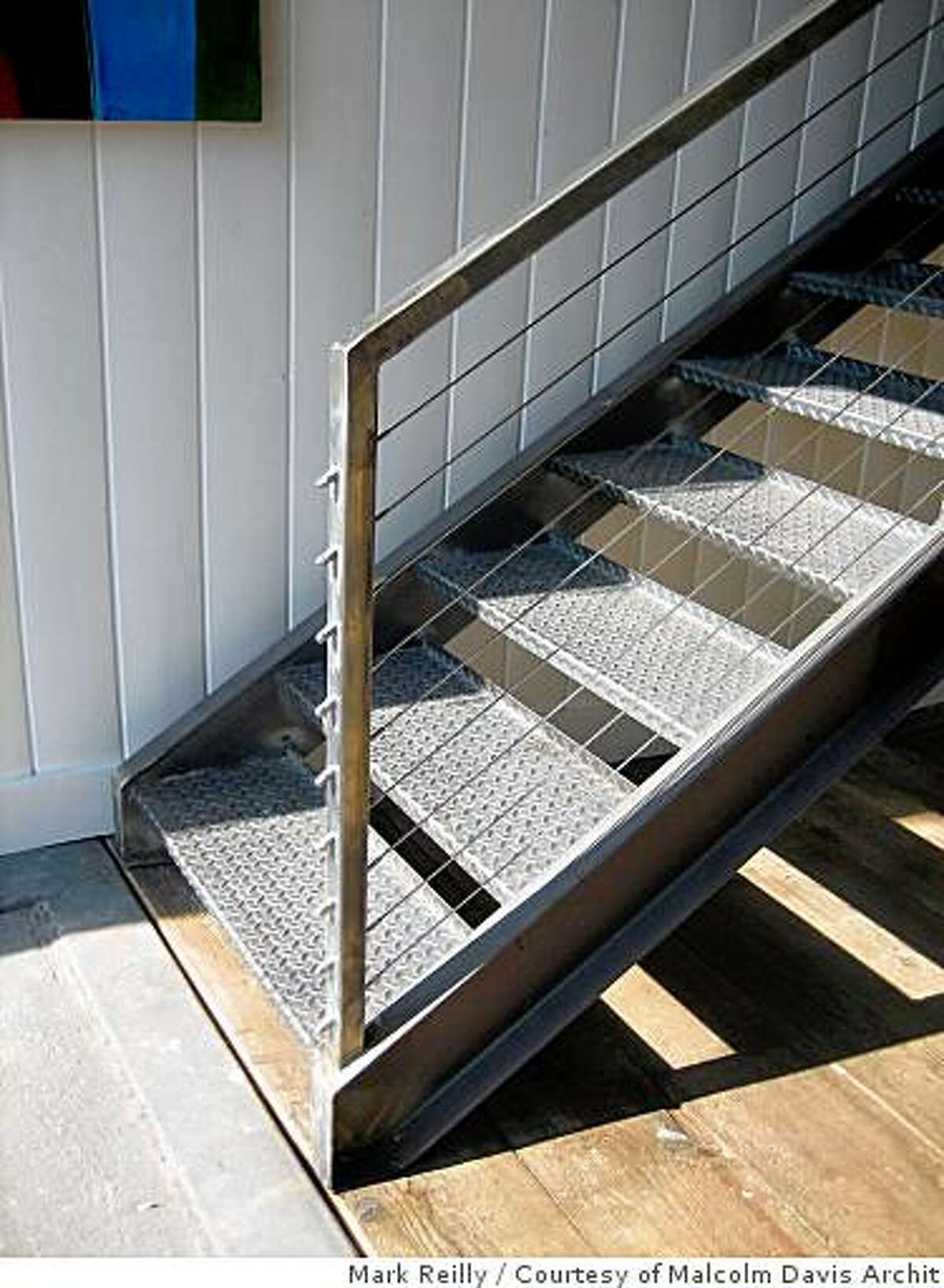 Custom steel stairs with cable railings insode The former carriagehouse in San Francisco's Missiopn district after architect Malcolm Davis completed spaces within it for several businesses, including a rental apartment, a commercial kitchen for caterers, a casual cafe called Stable and his own office, Malcolm Davis Architecture in the mezzanine and floor above. The building has a adjacent vacant lot that is used as a ciommunal courtyard.