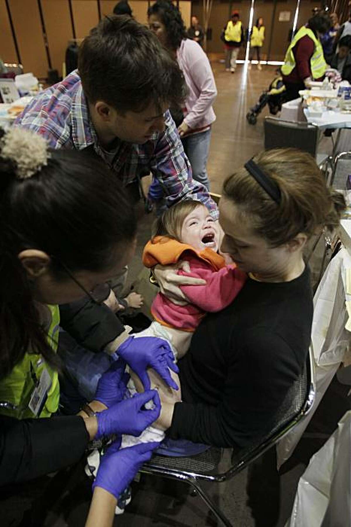 Lucy Jeffers, 1, receives a swine flu vaccine injection to her leg as her parents Crockett, top and Kate Jeffers hold her at the Bill Graham Civic Auditorium in San Francisco, Tuesday, Dec. 22, 2009. The city was administering 16,000 swine flu vaccinations Tuesday, the largest effort to date. (AP Photo/Marcio Jose Sanchez)