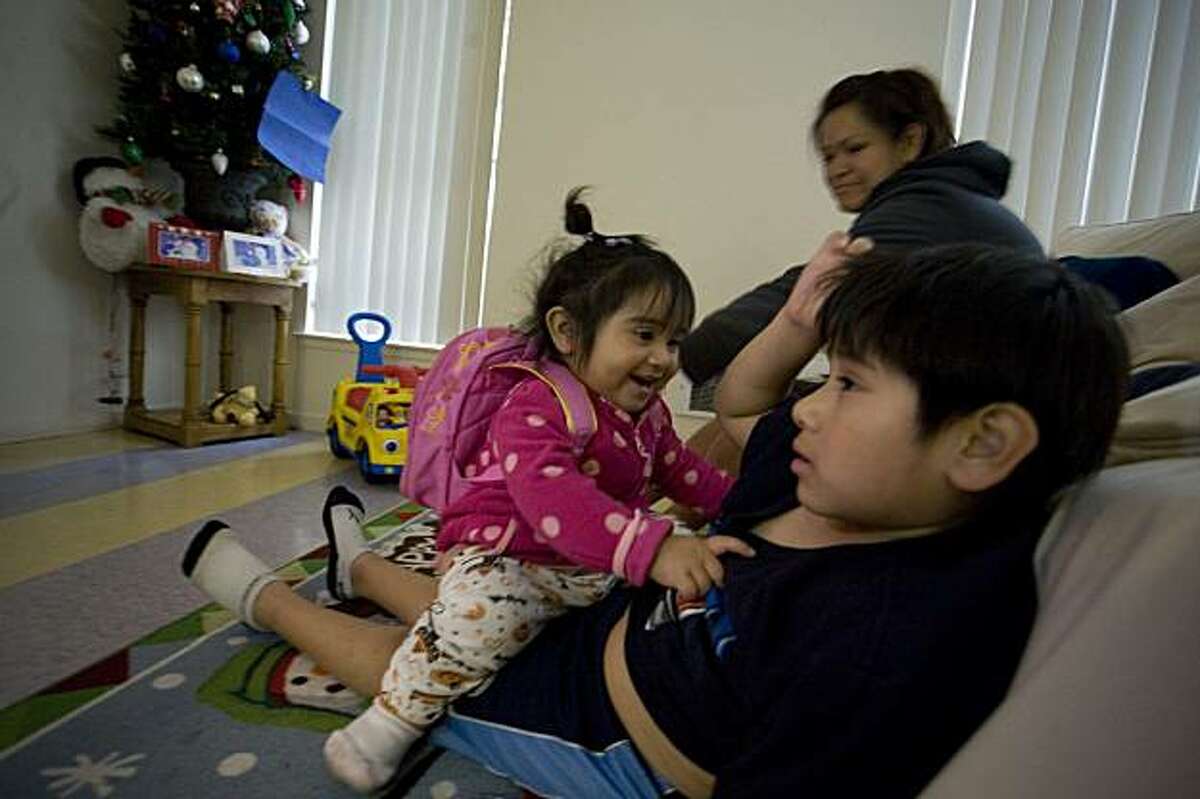 Stephanie Osorio, 18 mos., left, jumps on her six-year-old brother, Luis Osorio's lap to play in front of the family's Christmas tree at home in San Francisco, Calif. on Sunday, December 13, 2009. In the background, the children's mother, Alma Jimenez, stays at home with the kids while her husband, Erick Osorio (not pictured) is out looking for work. Kat Wade / Special to the Chronicle
