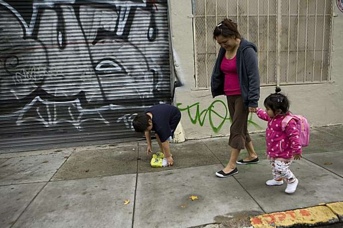 While his father is out looking for work, Luis Osorio, 6, puts on his Sponge Bob slipper that fell off while he and his mother, Alma Jimenez, and little sister, Stephanie Osorio, 18-mos., walk down Natoma Street near their new home in San Francisco, Calif. on Sunday, December 13, 2009. The Jimenez / Osorio family spent 6-months living in their van prior to finding low income housing at the Canon Barcus Community Housing complex in San Francisco. Kat Wade / Special to the Chronicle