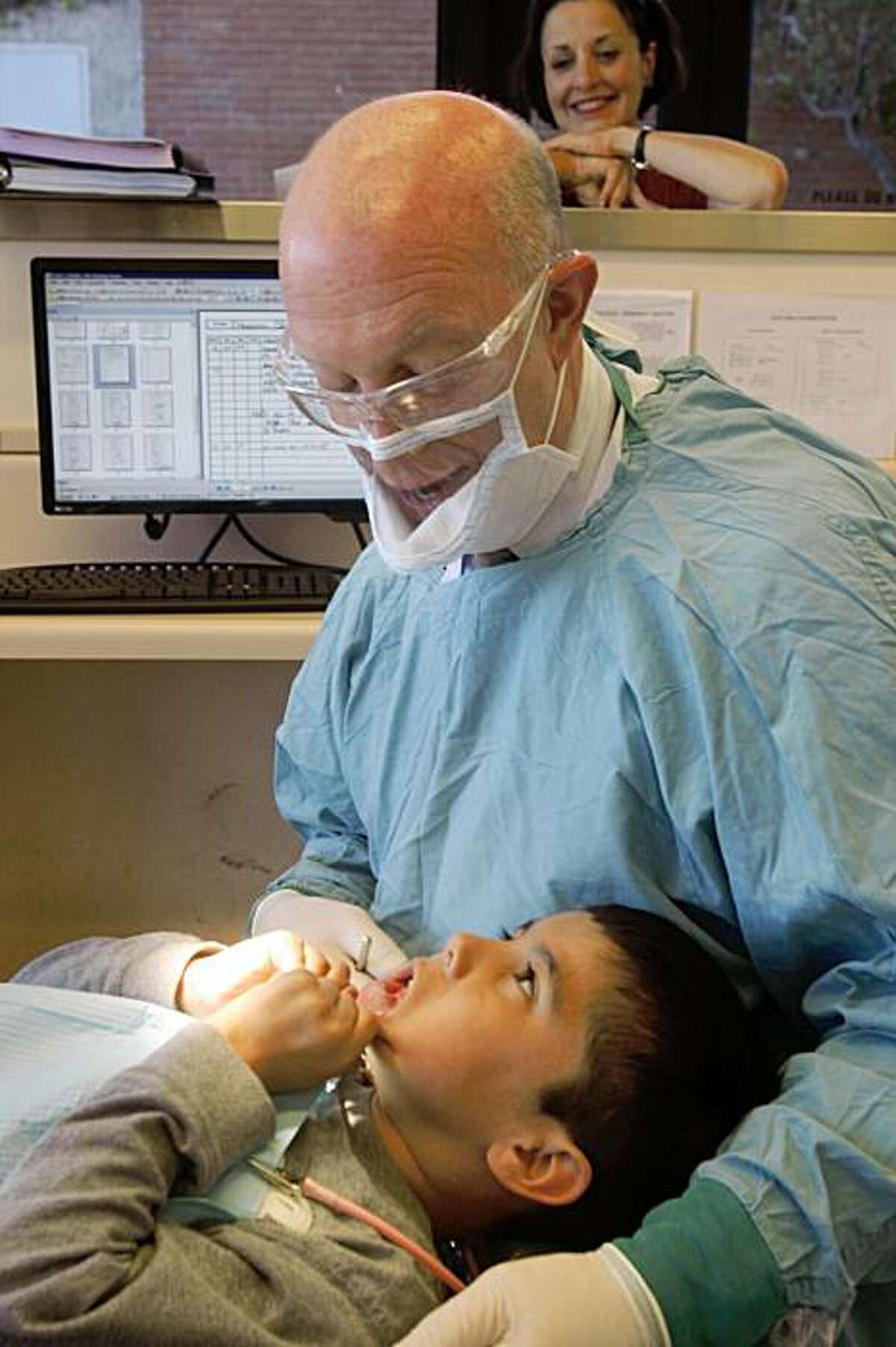Dr. Jeff Wood (left), professor of the University of the Pacific school of dentistry chatting with Christian Macias, 7 years old, on Tuesday morning, September 8, 2009, at the UOP dental school in San Francisco, Calif. In the background is RN Jeanne Hahne who invented a new see-through surgical mask and is testing the product at this dental office.