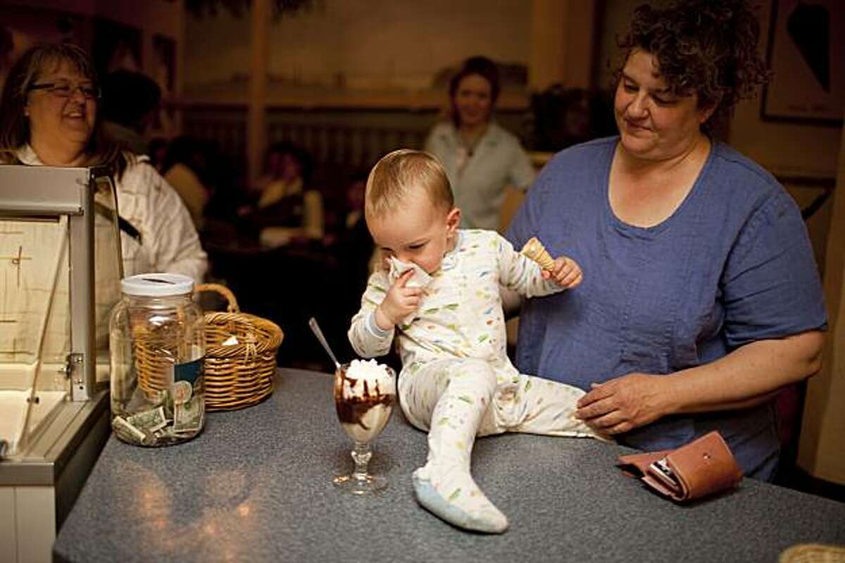 Watched by mother Schelle Simcox, right, 19 months-old Lukas Simcox, center, looks at a petite sundae at the counter of Tucker's Ice Cream in downtown Alameda, Calif. on Wednesday, Aug. 5, 2009.