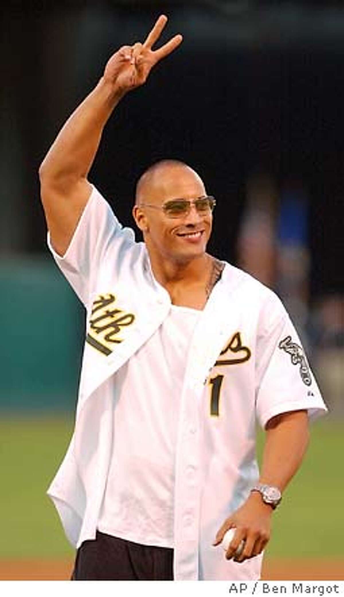 Wrestler turned actor "The Rock" flashes a peace sign to baseball fans prior to throwing out the first pitch of the game between the Anaheim Angels and Oakland Athletics Monday, Sept. 8, 2003, in Oakland, Calif. (AP Photo/Ben Margot)