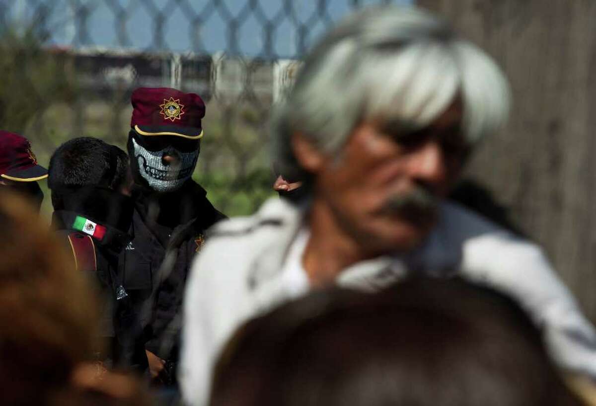 A state police officer wearing a face mask stands behind the fence as relatives of inmates wait for news after a prison riot at Apodaca correctional state facility in Apodaca on the outskirts of Monterrey, Mexico, Sunday Feb. 19, 2012. A fight among inmates at the prison led to a riot that killed dozens on Sunday, according to a security official.