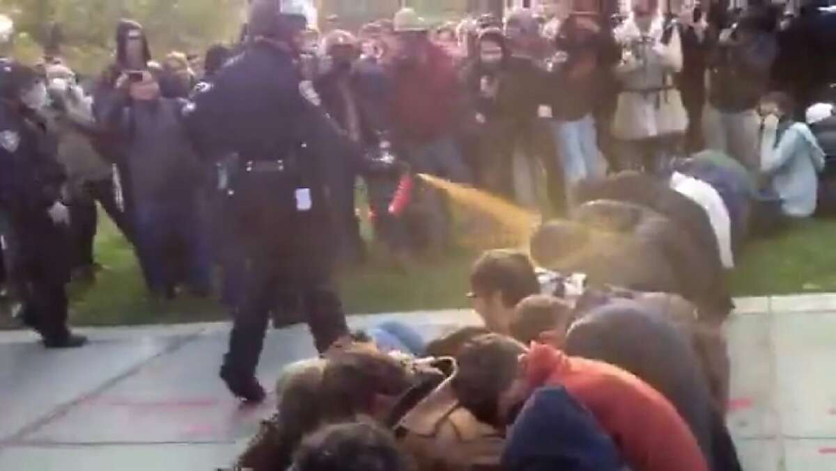 In this image made from video, a police officer uses pepper spray as he walks down a line of Occupy demonstrators sitting on the ground at the University of California, Davis on Friday, Nov. 18, 2011. The video - posted on YouTube - was shot Friday as police moved in on more than a dozen tents erected on campus and arrested 10 people, nine of them students. (AP Photo/Thomas K. Fowler)