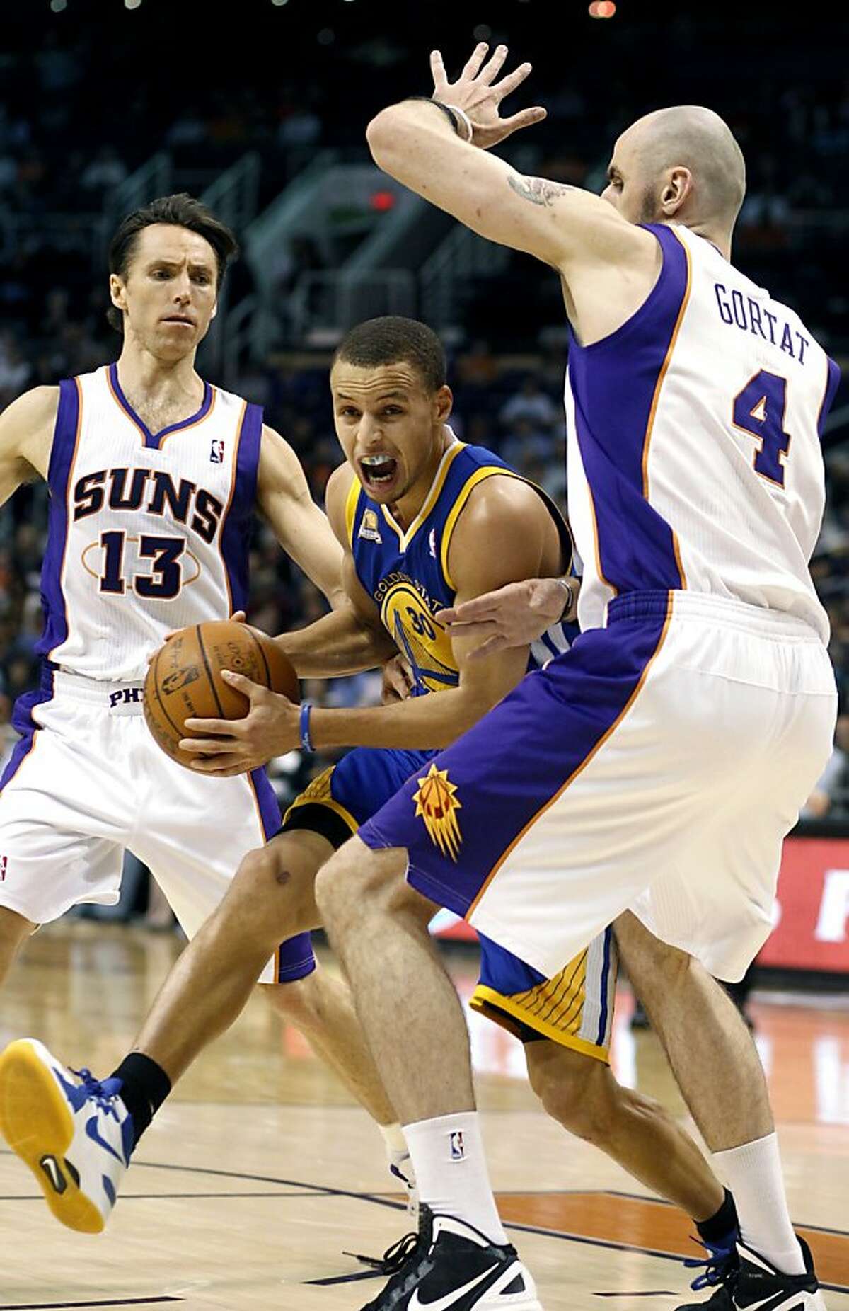 Golden State Warriors guard Stephen Curry, center, drives to the basket between Phoenix Suns guard Steve Nash, left, and center Marcin Gortat, right, of Poland, in the first quarter of an NBA basketball game Wednesday, Feb. 22, 2012, in Phoenix.