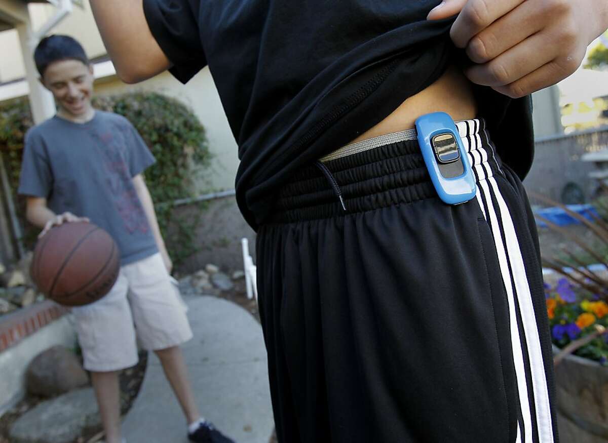Tristan Wegman shows off the Zamzee device which is so small it is hidden under his t-shirt. His friend Steven Effisimo stands in the background. Tristan Wegman of Redwood City, Calif. uses the Zamzee device to measure his exercise on a daily basis. He also checks his exercise numbers in a fun format online.