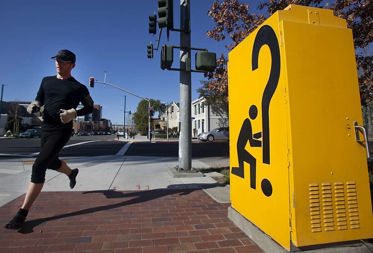 A jogger runs past a "Signs of the Times" electrical box on Park Avenue on Saturday morning in Emeryville. Emeryville's Art in Public Places program features sculptures by local artists that are scattered throughout the city. Pieces like "Signs of the Times," sit on street corners, local businesses, and parks.