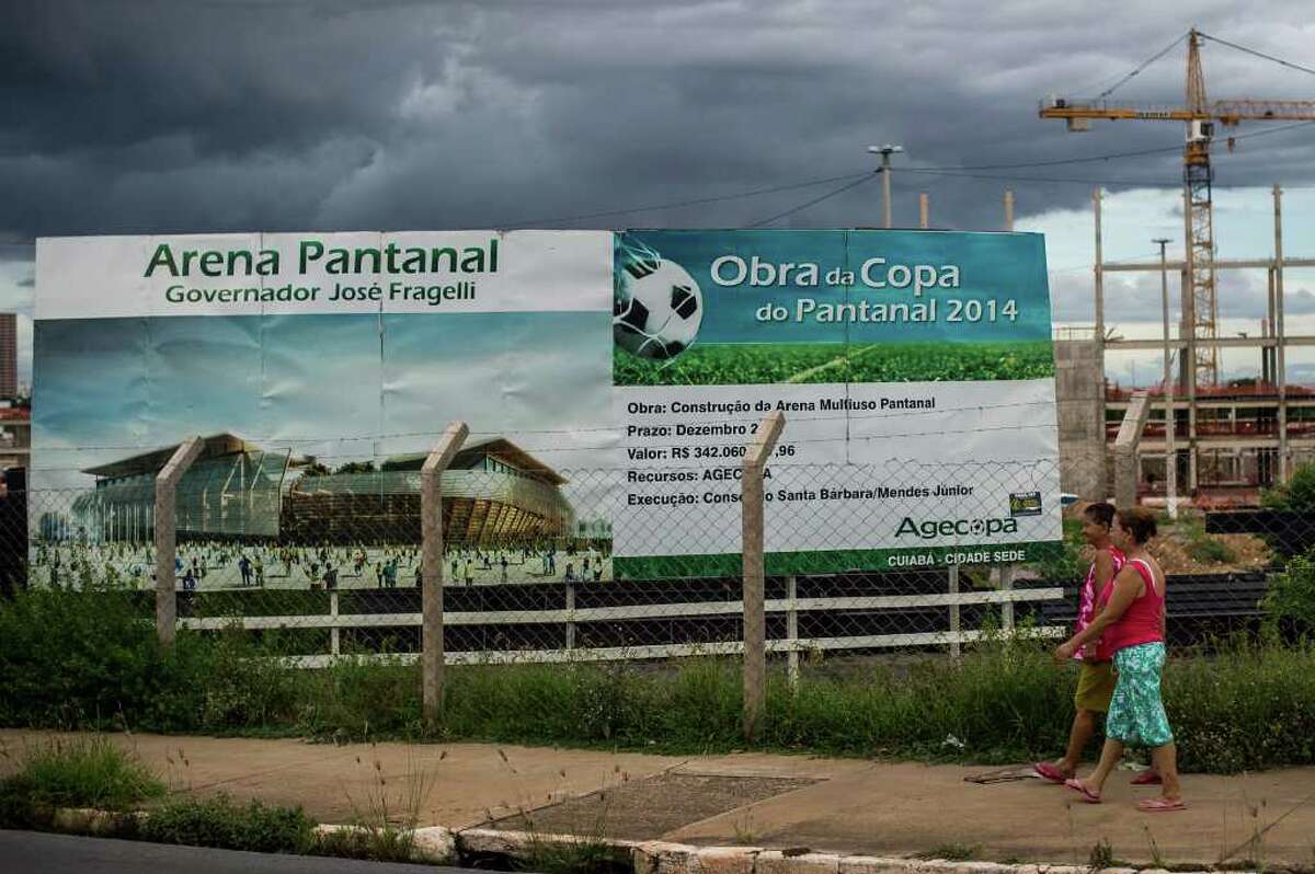 People pass by a billboard of a new stadium for the FIFA World Cup 2014, Arena Pantanal, at the construction site after an old stadium was demolished in Cuiaba, Mato Grosso State, Brazil on January 29, 2012. AFP PHOTO/Yasuyoshi CHIBA (Photo credit should read YASUYOSHI CHIBA/AFP/Getty Images)