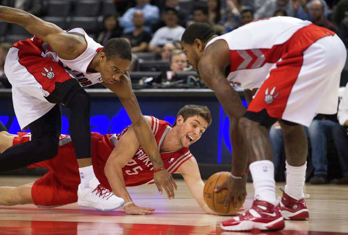 Toronto Raptors guard DeMar DeRozan, left, and forward Amir Johnson, right, reach for the loose ball against Houston Rockets forward Chandler Parsons during the first half of an NBA basketball game in Toronto on Wednesday, March 7, 2012. (AP Photo/The Canadian Press, Nathan Denette)
