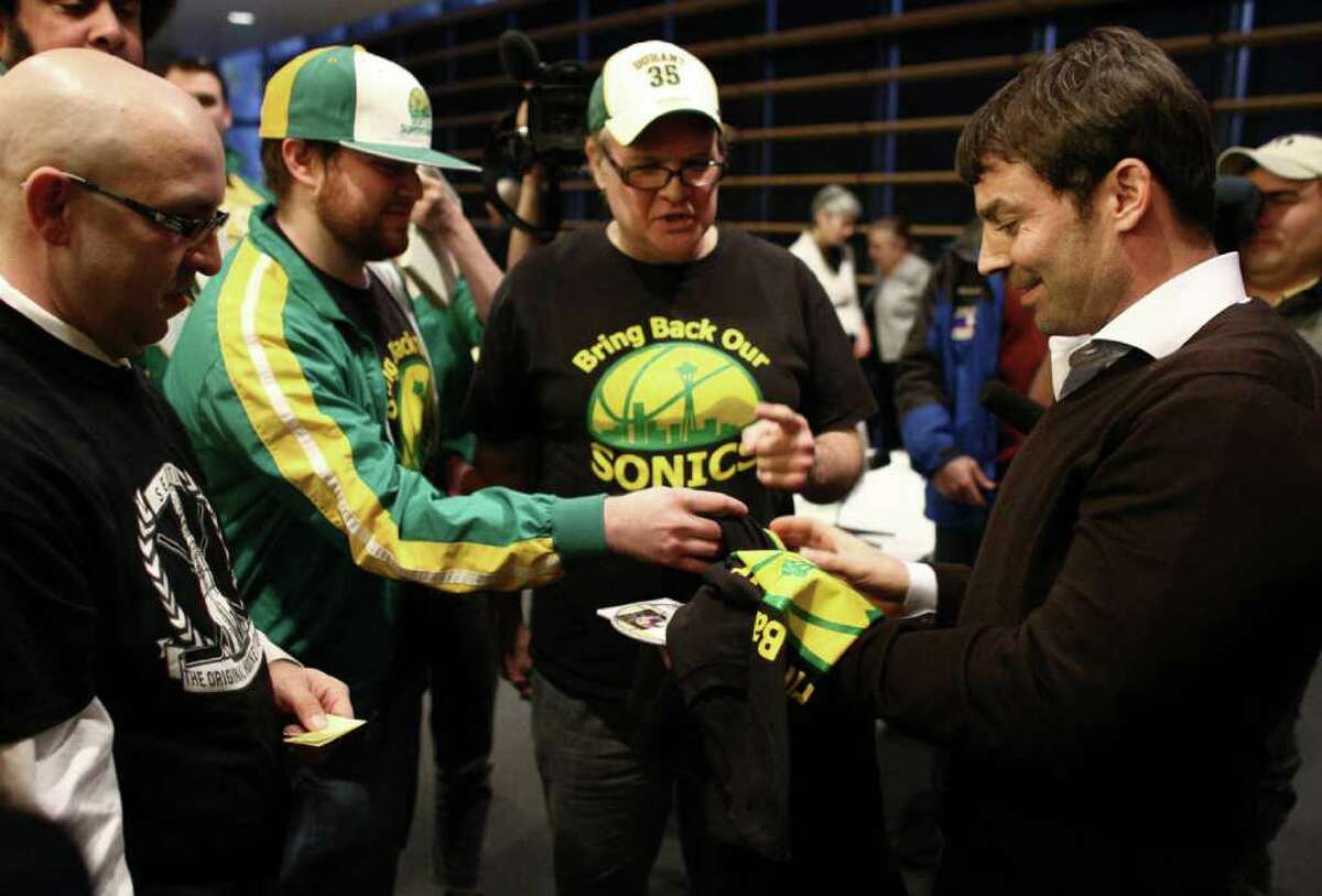 Bring Back Our Sonics co-founders David Brown, center, and Jeff Brown, left, present T-shirts to Seattle native Chris Hansen, who is leading a group of investors to bring a NBA and NHL team to Seattle. Hansen spoke before the Arena Review Panel on Wednesday, March 7, 2012 at Seattle City Hall.