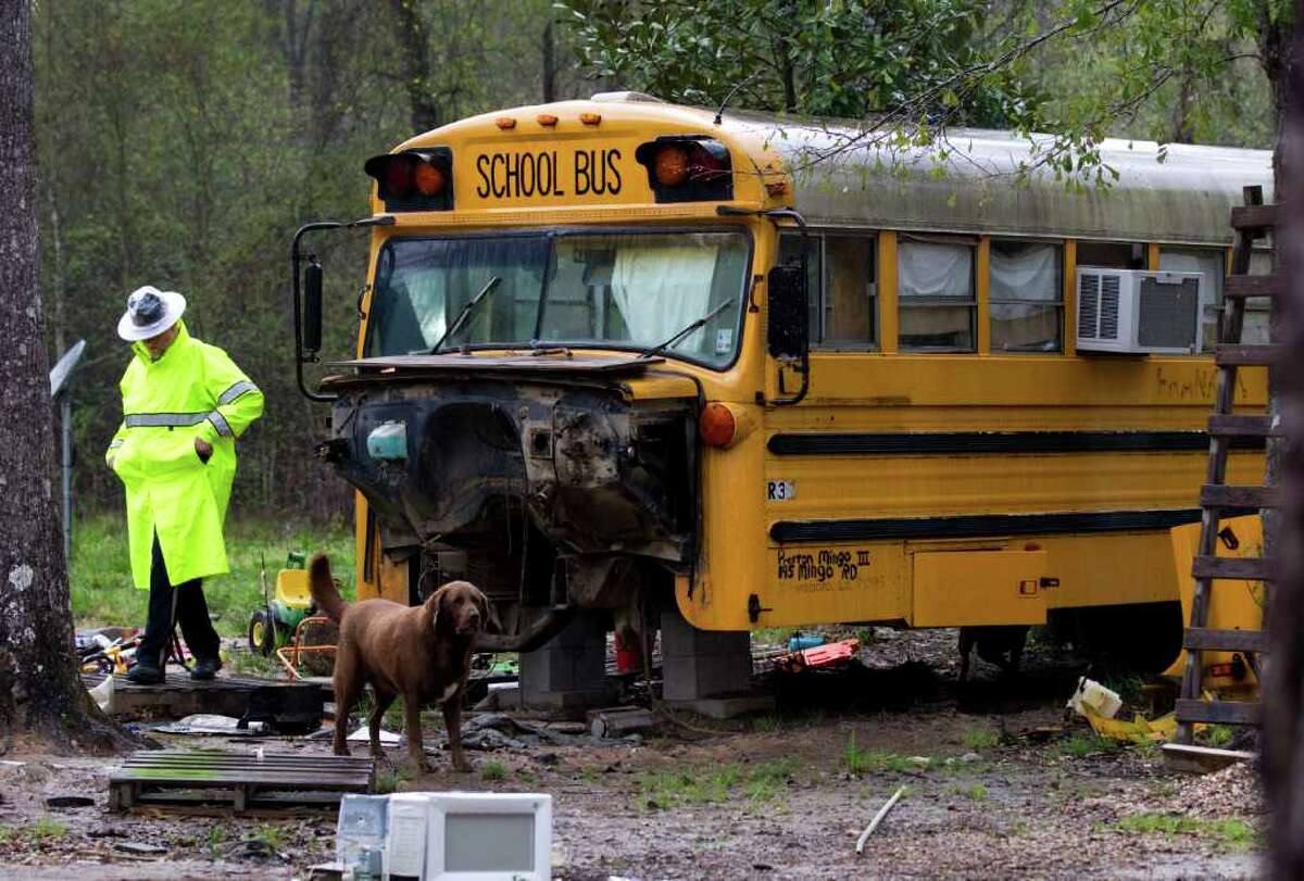 A Montgomery County sheriff's deputy steps through trash and junk surrounding an old school bus where two young children were found living unsupervised Wednesday in Splendora. The 11-year-old girl and her brother, 5, were taken into protective custody.