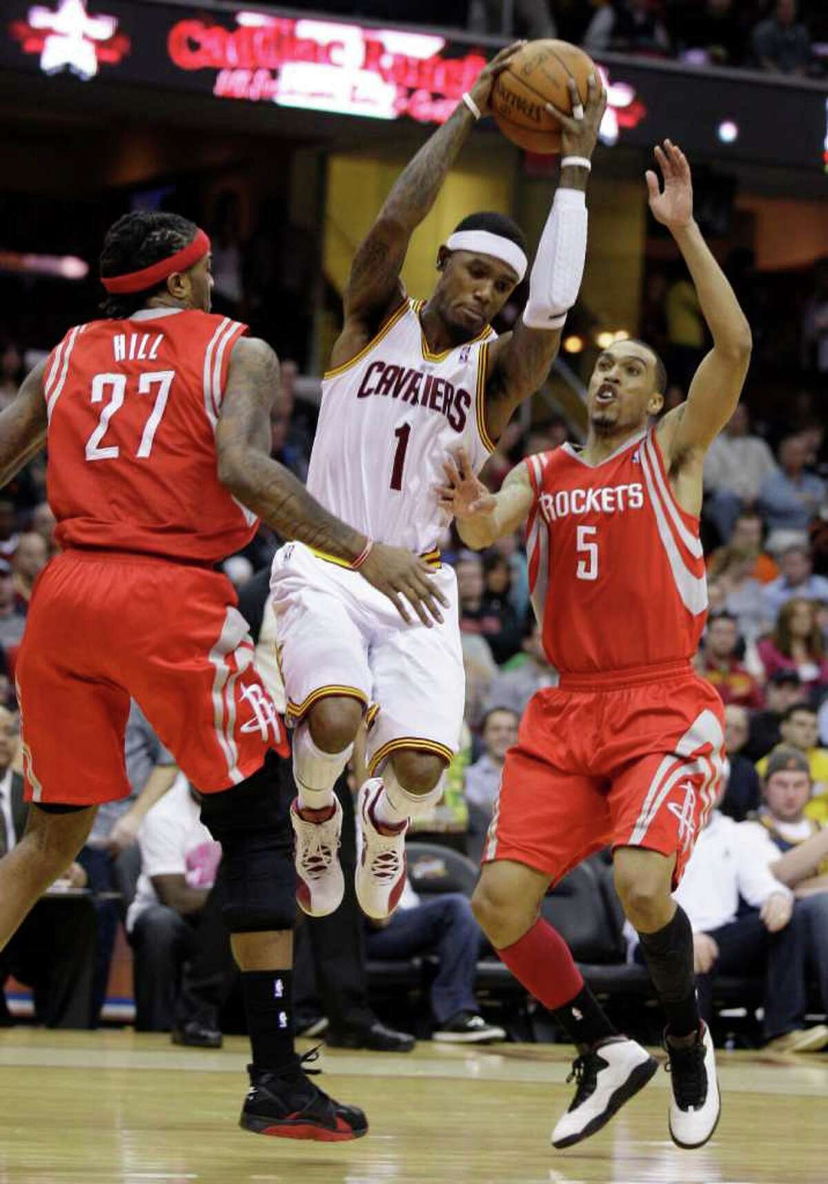 Cleveland Cavaliers' Daniel Gibson (1) jumps between Houston Rockets center Jordan Hill (27) and Courtney Lee (5) in the first quarter in an NBA basketball game Sunday, March 11, 2012, in Cleveland. (AP Photo/Tony Dejak)