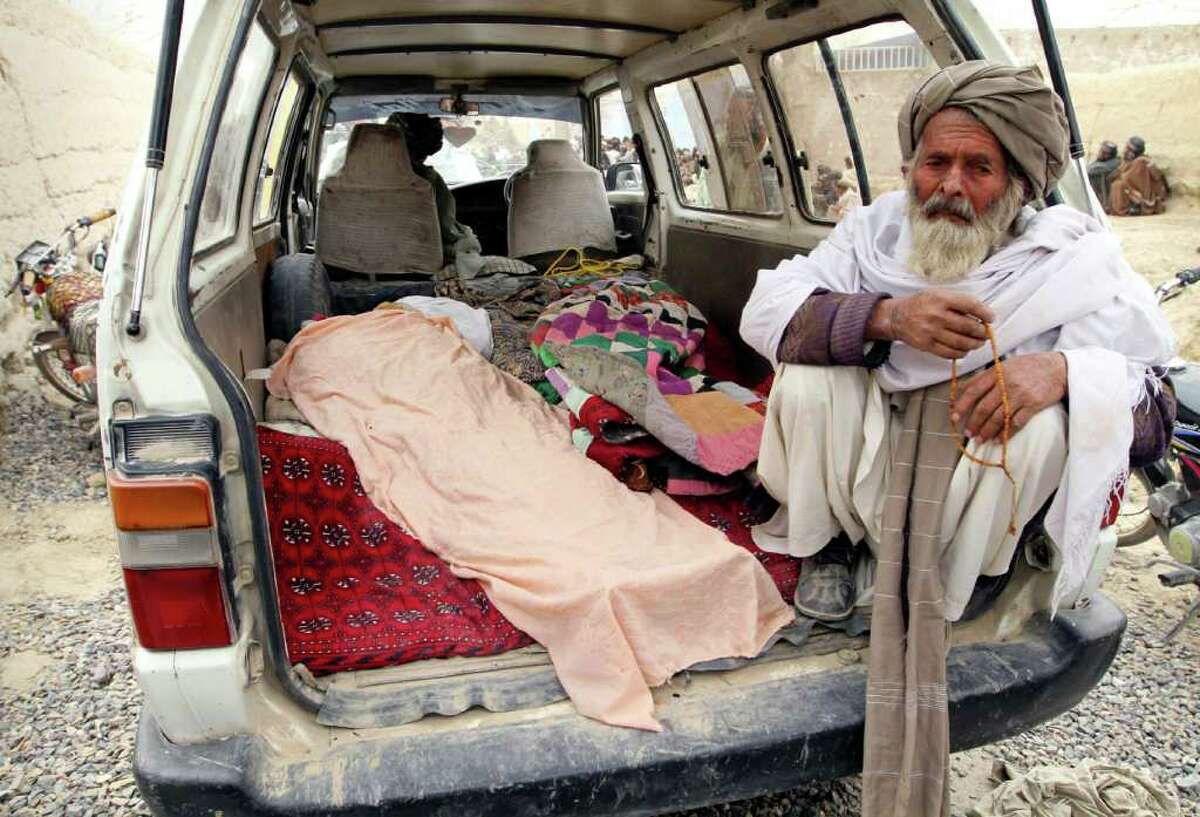 An elderly Afghan man sits next to a covered body, who was allegedly killed by a U.S. service member, in a minibus in Panjwai, Kandahar province south of Kabul, Afghanistan. (AP Photo/Allauddin Khan)