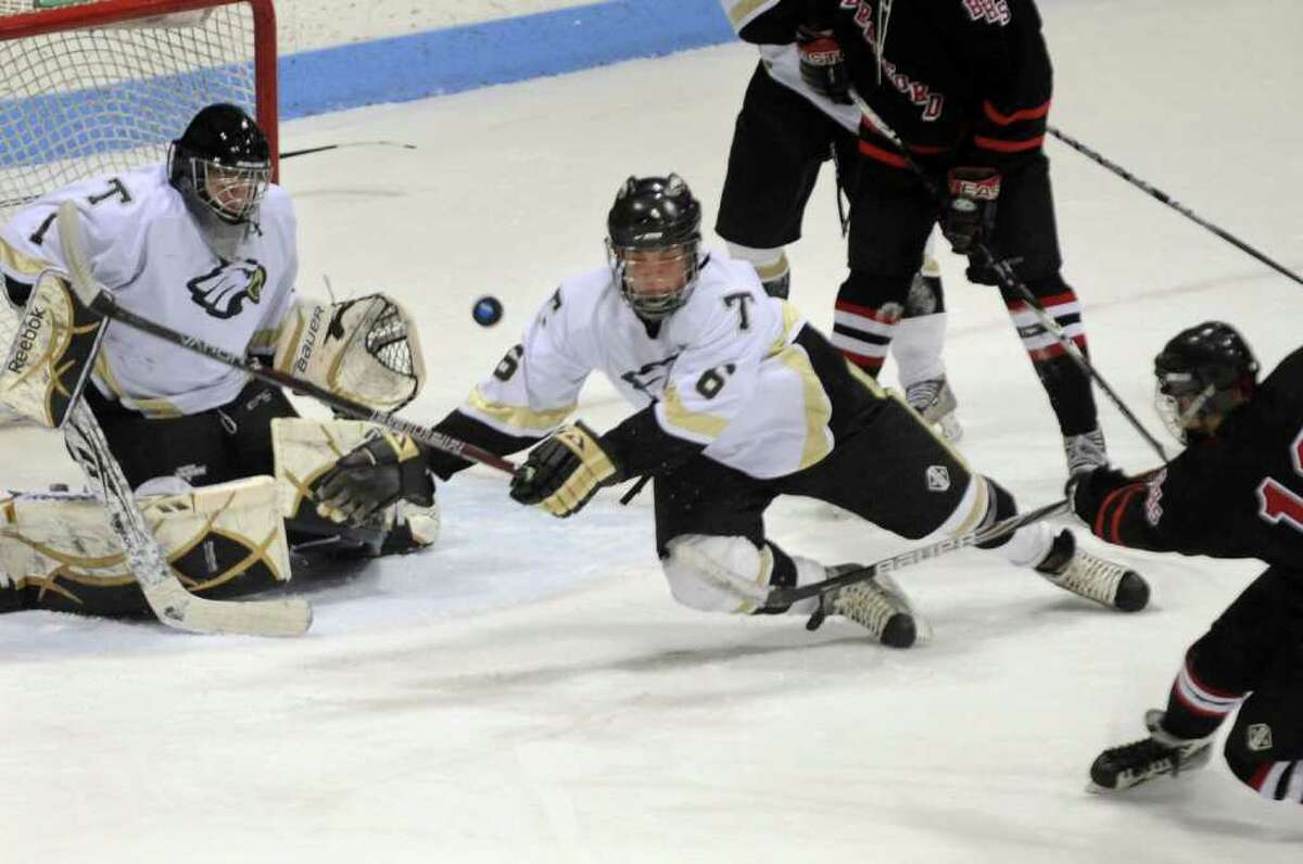 Trumbull"s #6 Cory Watson leaps in to try and stop a shot by Branford's #13 Tony Pascale, right, during Division II boys ice hockey state final action in New Haven, Conn. on Friday March 16, 2012. At left is goalie Matthew Paolini.