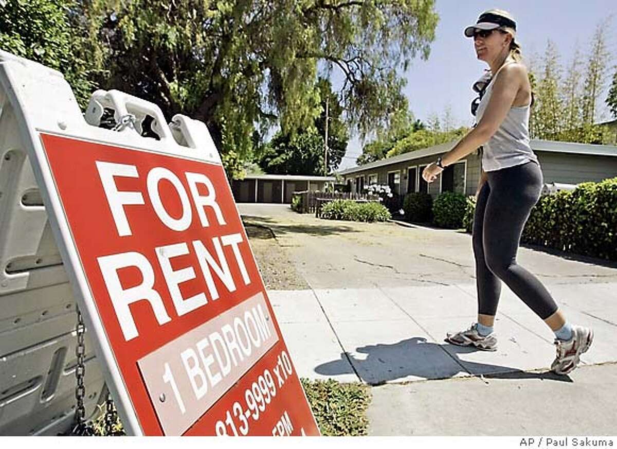 A woman walks next to a "For Rent" sign at an apartment complex in Palo Alto.