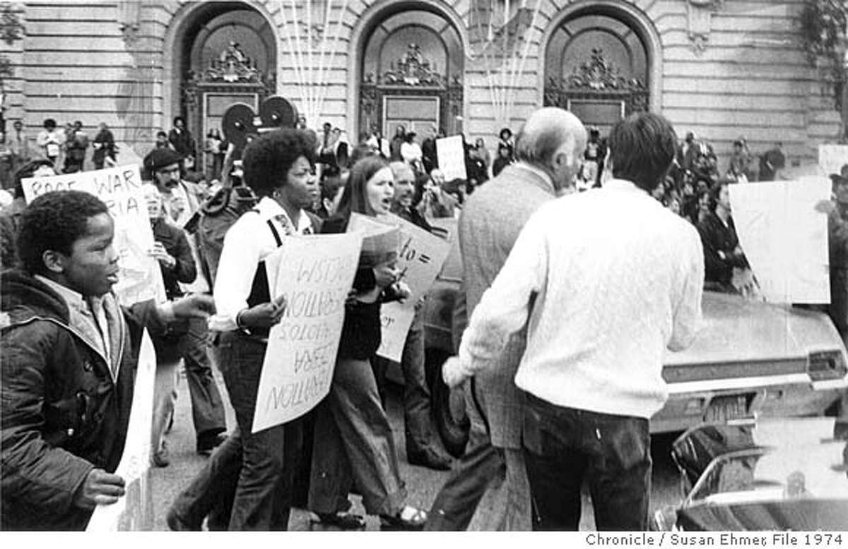 ZEBRAMURDER-22APR1974-SE - Mayor Joe Alioto, on his way to his card outside of City Hall. Protesters of the Zebra Murders, holding signs, follow him. Photo by Susan Ehmer