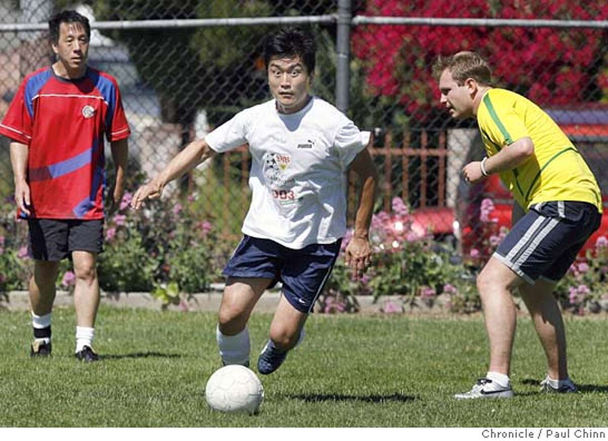 Peter Oh dribbles past Donavan Tom (left) and Onur Kaya (right) during a weekly pick-up game at a park in Berkeley, Calif. on Saturday, June 3, 2006. Soccer fans around the Bay Area are gearing up for the World Cup tournament which is about to begin in Germany later this month. PAUL CHINN/The Chronicle **Peter Oh, Donavan Tom, Onur Kaya