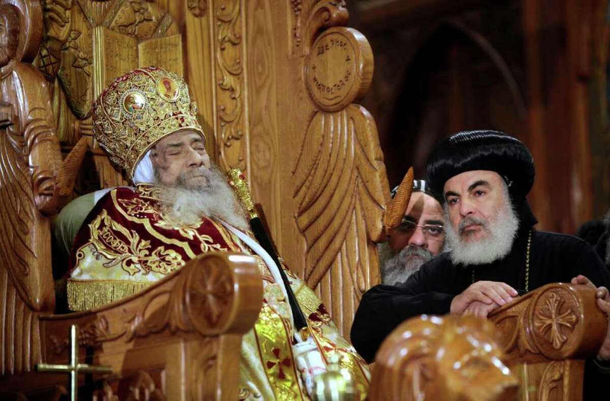 Archbishops stand next to the body of Pope Shenouda III is seated on the throne of Mar Morqos, or St. Mark, as mourners gather for the viewing of the patriarch at the Coptic Orthodox Church in Cairo, Egypt, Sunday, March 18, 2012. (AP Photo/Amr Nabil)