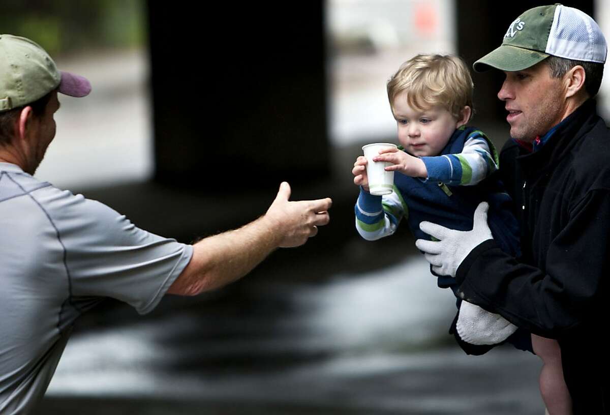 George Saunders, 2, with Coach Art, hands a cup of water to a marathon runner on Sunday at Broadway in Oakland. Marathon runners faced a 26 mile trek through Oakland on Sunday during the annual Oakland Running Festival. The race started at 7:30 am at Snow Park, and tread through areas such as Montclair, Moon Temple, and Lake Temescal.