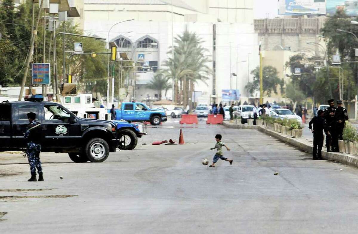 A child plays soccer as Iraqi security forces guard a street in central Baghdad, Iraq, Wednesday, March, 28, 2012. The Iraqi government has tightened its security measures for the Arab League summit in Baghdad. (AP Photo/Khalid Mohammed)