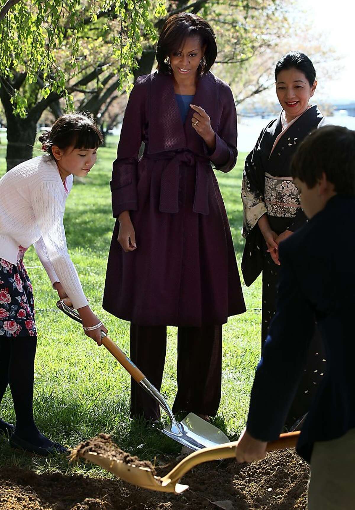 U.S. first lady Michelle Obama (C) takes part in a 1912 Cherry Blossom tree planting re-enactment ceremony with Yoriko Fujisaki (R) near the Tidal Basin and along the Potomac River March 27, 2012 in Washington, DC. 2012 marks the 100th anniversary since the United States received 3,000 Cherry Blossom trees as a gift from Japan symbolizing the friendship between the two countries.