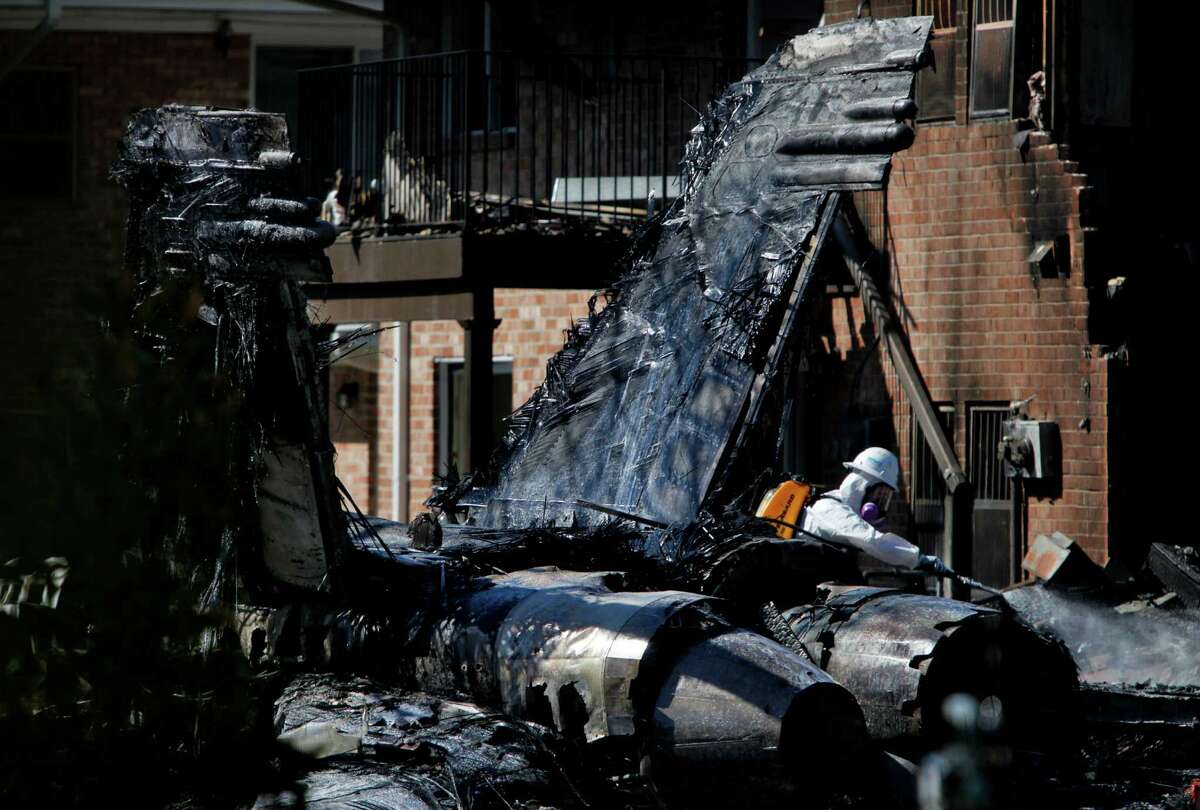 Hazardous materials workers spray down the remains of an F/A-18D Hornet jet that crashed Friday at Mayfair Mews apartments in Virginia Beach, Va., on Saturday, April 7, 2012.