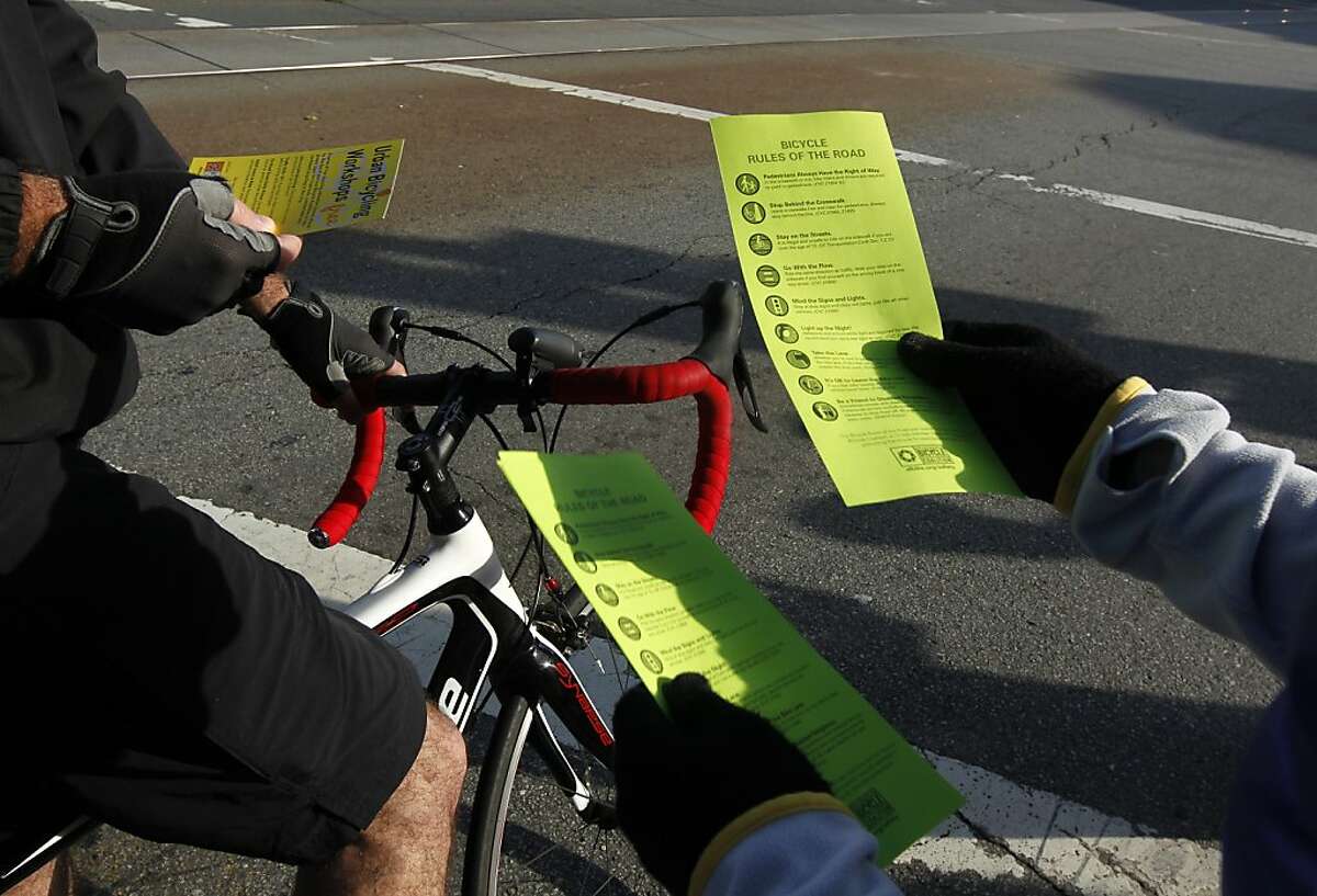 A volunteer from the San Francisco Bicycle Coalition distributes the organization's Rules of the Road to cyclists commuting on Market Street in San Francisco, Calif. on Friday, April 6, 2012.