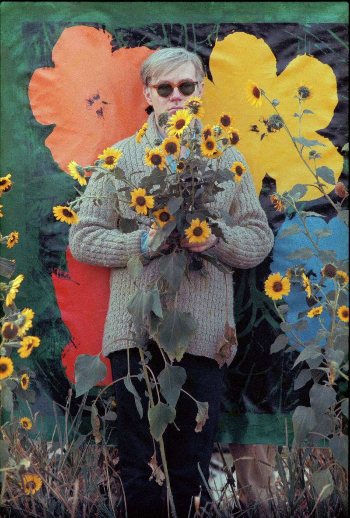 In this 1964 photo provided by Allen Cooper Enterprises, artist Andy Warhol stands in a field of Black-Eyed Susans in New York. The image will be featured in an exhibit entitled: "Before They Were Famous: Behind the Lens of William John Kennedy," which opens on April 19th at the Site/109 gallery in New York. (AP Photo/William John Kennedy via Allen Cooper Enterprises)