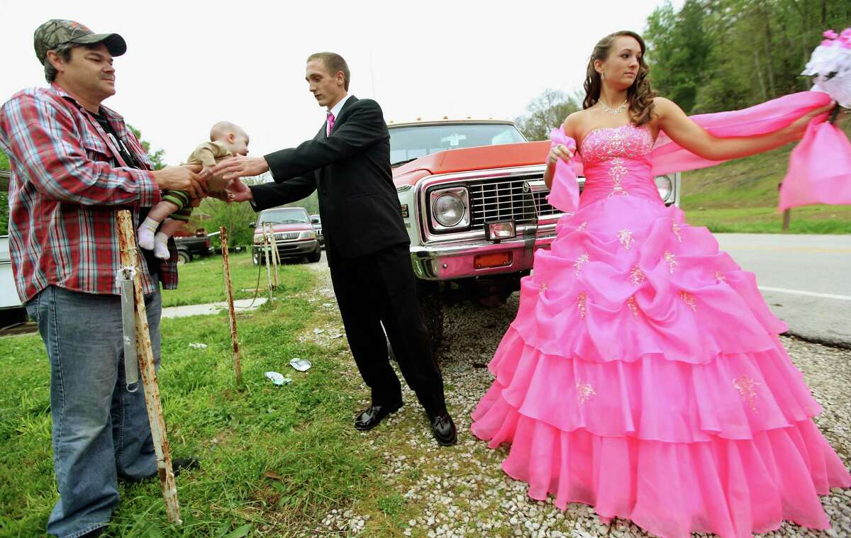 Dates Coty Shouse (C) and Destiny Duff (R) gather as Destiny's father Ronnie Duff (L) passes a baby to be photographed while preparing for the Owsley County High School prom on April 21, 2012 in Booneville, Kentucky.