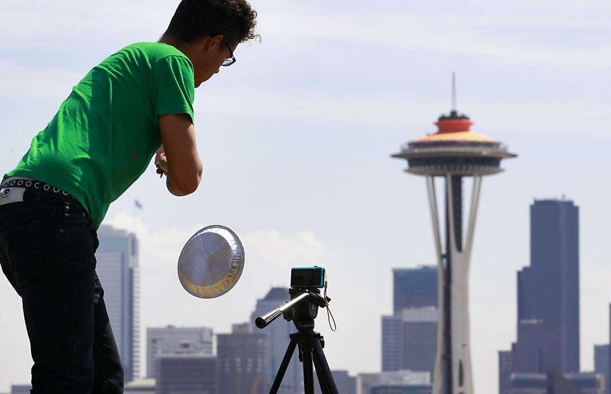 Traeden Mathews dangles a pie tin in front of a tiny video camera and in view of the Space Needle as he films an extremely low-budget film about space invaders landing on Earth Monday, April 23, 2012, in Seattle. He was producing the tongue-in-cheek film for a friend's birthday. The top of the Space Needle behind sports a new coat of orange, called "galaxy gold" when it first appeared 50 years ago atop the structure, as part of the landmark's 50th anniversary celebration. The Space Needle, 605 feet tall, officially opened on the first day of the World's Fair April 21, 1962. (AP Photo/Elaine Thompson)