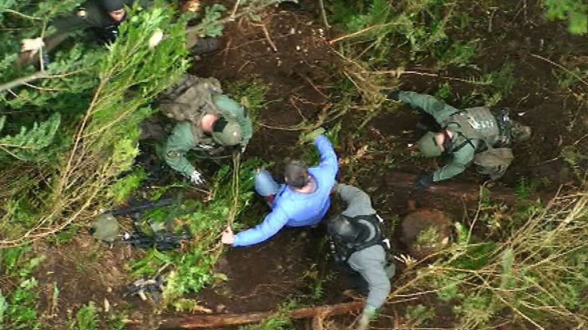 In this still frame taken from video provided by the King Co. Sheriff's Dept., a detective, center, is helped to the ground by other law-enforcement officers after he was lowered from a helicopter to an area near a deep-woods bunker, Saturday, April 28, 2012, in North Bend, Wash. Police, who had surrounded the bunker since Friday, found a dead body inside on Saturday. Authorities earlier said they believed that Peter A. Keller, who is suspected of killing his wife and daughter last week, was hiding out in the bunker.