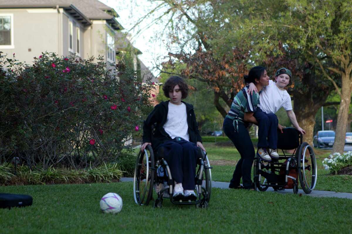 Wendy Ortiz, who has been Aaron and Peter's caretaker since Aaron was 8 months old, lifts Aaron, 9, out of his wheel chair so he could play ball with his brother Peter, 10, left, and his cousins in the front yard where they live with their aunt and uncle Monday, March 12, 2012, in Houston.