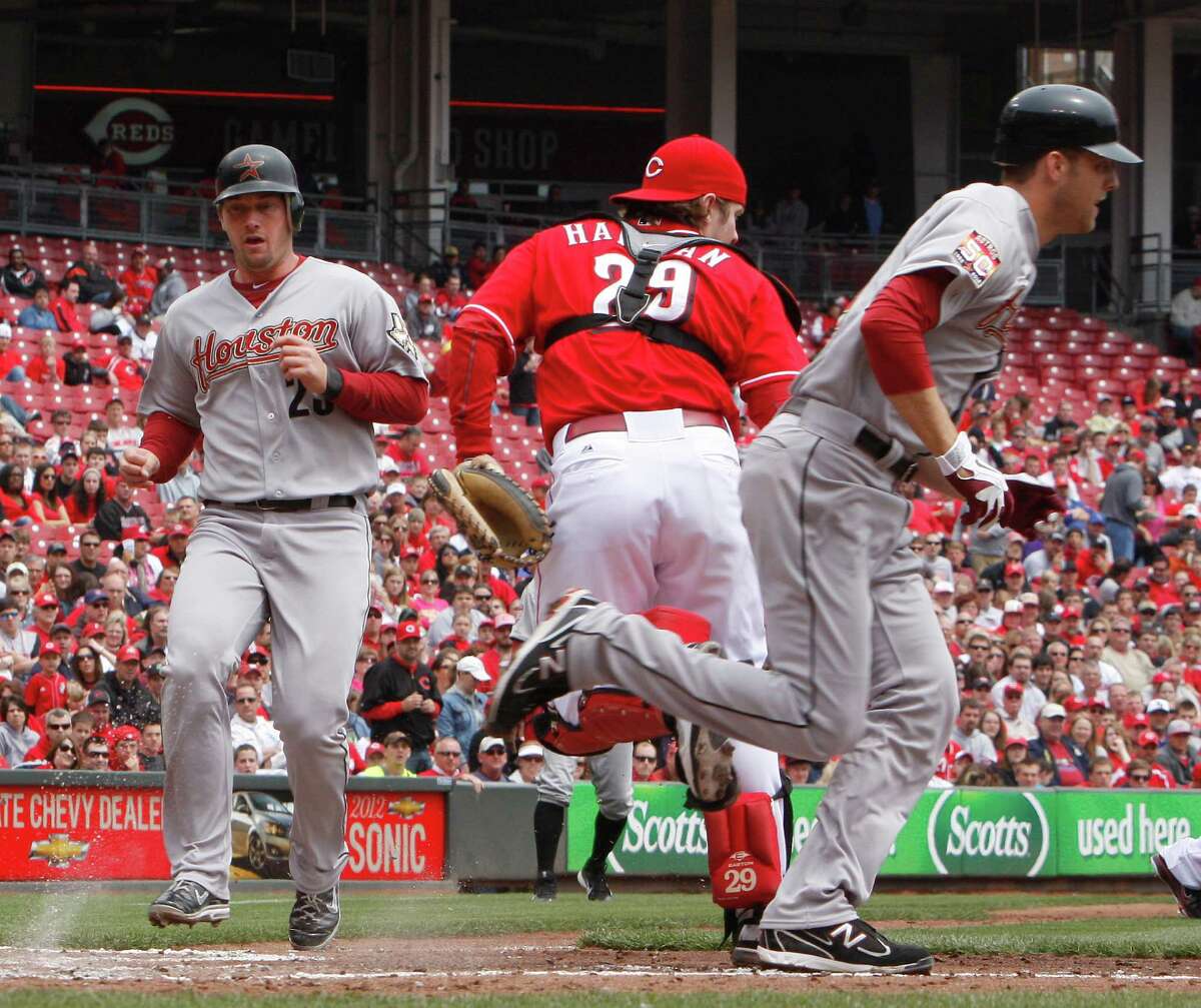Houston Astros' Jordan Lyles, right, bunts as teammate Chris Johnson, left, scores during the second inning of a baseball game against the Cincinnati Reds, Sunday, April 29, 2012, in Cincinnati. Reds catcher Ryan Hanigan, center, awaits the throw. The Reds came from behind to win 6-5. (AP Photo/David Kohl)