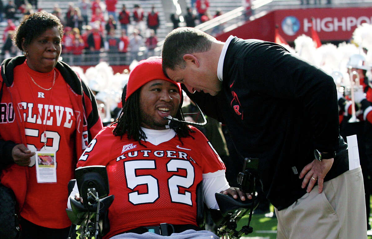 FILE - In this Nov. 19, 2011 file photo, paralyzed former Rutgers football player Eric LeGrand, center, is greeted by coach Greg Schiano, right, before an NCAA college football game against Cincinnati in Piscataway, N.J. Eric's mother, Karen LeGrand, looks on at left. LeGrand has been signed by the Tampa Bay Buccaneers. LeGrand broke two vertebrae and suffered a serious spinal cord injury on Oct. 16, 2010 during a kickoff return against Army. His coach at Rutgers then, now is coach of the Bucs. (AP Photo/Home News Tribune, Mark R. Sullivan) NEWARK OUT; NO SALES